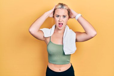 Spor kıyafetleri ve havlu giyen genç sarışın kız çıldırmış ve elleri başının üstünde korkmuş, korkmuş ve ağzı açık şoktan şaşırmış. 