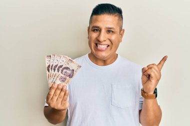 500 Meksika pezosu tutan genç Latin adam gülümsüyor mutlu bir şekilde elini ve parmağını kenarda gösteriyor. 
