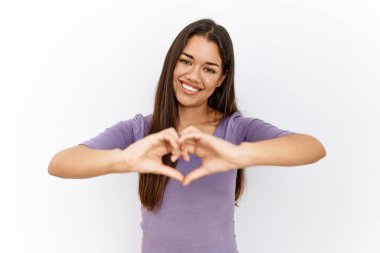 Genç esmer kadın izole edilmiş arka planda duruyor. Sevgiyle gülümsüyor. Elleriyle kalp sembolü yapıyor. romantik kavram. 