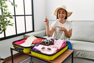 Güzel, orta yaşlı İspanyol bir kadın valize yazlık giysiler yerleştiriyor gülümsüyor ve kameraya bakıyor iki eliyle ve parmaklarıyla yan tarafa bakıyor.. 