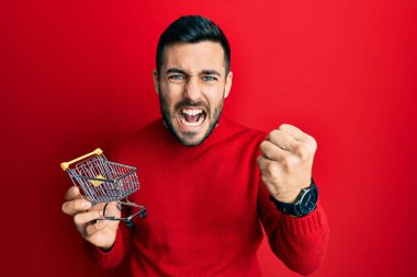 Küçük bir süpermarket arabası tutan İspanyol genç adam öfkeyle bağırıyor, öfkeyle bağırıyor ve el kaldırıyor. 