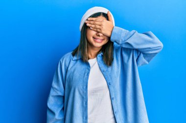 Şirin yün şapkalı, gülümseyen ve gülen genç Latin kadın şaşırmak için gözlerini kapatıyor. kör kavram. 