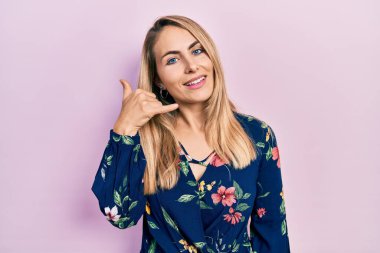 Sıradan kıyafetler giyen, gülümseyen, el ve parmaklarıyla telefon hareketi yapan, telefonda konuşan beyaz bir kadın. iletişim kavramları. 