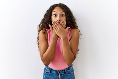Güzel İspanyol kadın izole edilmiş arka planda dikiliyor. Ağzını yanlışlıkla ellerle kapatıyor. gizli kavram. 