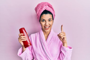 Duş bornozu giymiş, elinde şampuanla gülümseyen genç İspanyol kadın bir fikir veya soruyla mutlu bir yüzü işaret ediyor. 