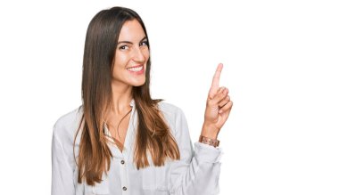 Yüzünde kocaman bir gülümseme olan sıradan kıyafetler giyen genç ve güzel bir kadın, kameraya el ile işaret ederek bakıyor.. 