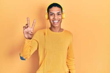 Genç Afro-Amerikalı adam müzik dinliyor kulaklıkla gülümsüyor kameraya bakıp zafer işareti yapıyor. İki numara.. 