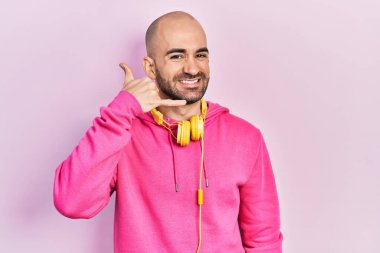 Spor kıyafetleri giyen, kulaklık takan, gülümseyen, el ve parmaklarıyla telefonla konuşan kel bir adam. iletişim kavramları. 