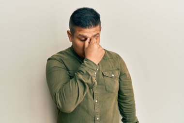 Gündelik kıyafetler giyen genç latin adam yorgun burnu ve gözleri ovuşturuyor yorgunluk ve baş ağrısı hissediyor. Stres ve hüsran kavramı. 