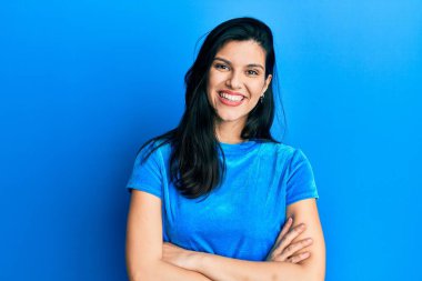 Gündelik kıyafetler giyen, kollarını kavuşturup kameraya gülümseyen genç İspanyol kadın. pozitif kişi. 