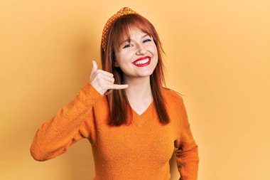 Kızıl saçlı, turuncu süveter giyen, gülümseyen, el ve parmaklarıyla telefonla konuşan genç bir kadın. iletişim kavramları. 