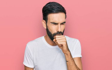 Günlük beyaz tişört giyen İspanyol genç adam kendini iyi hissetmiyor ve soğuk algınlığı veya bronşitin belirtisi olarak öksürüyor. sağlık hizmeti kavramı. 