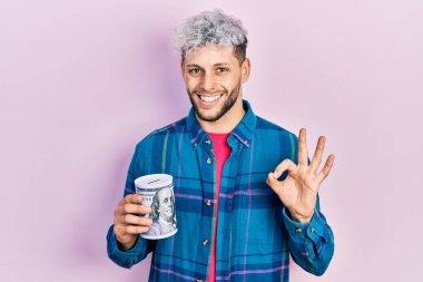 Modern boyalı saçlı, kumbaralı genç İspanyol adam parmaklarıyla imza atıyor, gülümseyerek mükemmel bir sembol oluşturuyor. 