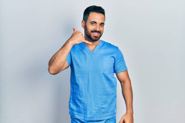 Sakallı, mavi erkek hemşire üniforması giyen, telefonda el ve parmaklarıyla telefonla konuşan yakışıklı İspanyol bir adam. iletişim kavramları. 
