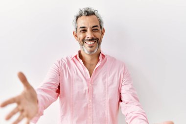 Orta yaşlı İspanyol bir adam izole edilmiş arka planda durup kameraya bakarak sarılmak için kollarını açmış gülümsüyor. Mutluluğu kucaklayan neşeli bir ifade.. 