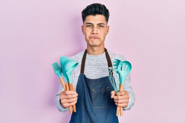 Profesyonel fırıncı önlüğü giyen genç İspanyol adam elinde yemek aletleri tutuyordu. Depresyondaydı ve sıkıntıdan endişe ediyordu. Öfkeli ve korkmuştu. hüzünlü ifade. 