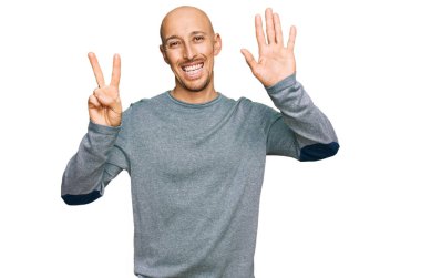 Kel, sakallı, günlük giysiler giymiş yedi numaralı parmaklarıyla gösteriş yapan, kendinden emin ve mutlu bir şekilde gülümseyen bir adam.. 