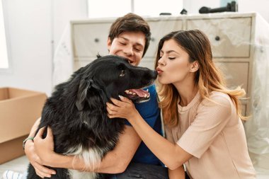 Genç beyaz çift mutlu bir şekilde gülümsüyor. Yeni evlerinde yerde köpekleriyle oturuyorlar..