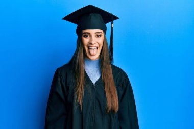 Mezuniyet şapkası ve tören cübbesi takan güzel esmer bir kadın komik bir ifadeyle dilini dışarı çıkarıyor. duygu kavramı. 