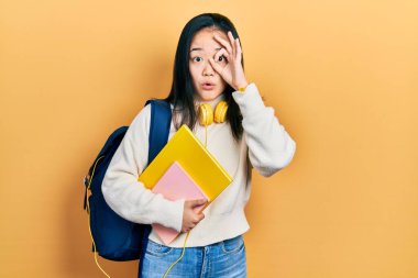 Öğrenci çantası ve kitapları tutan genç Çinli kız şaşırmış yüz ifadesiyle şaşırmış, parmaklarından bakan gözler. İnançsız ifade. 