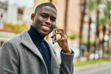 Genç Afrikalı Amerikalı gülümseyen mutlu bir adam şehirdeki akıllı telefondan konuşuyor.