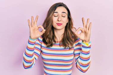 Gündelik kıyafetler giyen, gözleri kapalı gülümseyen genç İspanyol kız parmaklarıyla meditasyon hareketi yapıyor. yoga konsepti. 