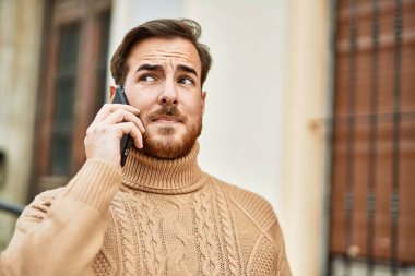 Ciddi bir suratı olan beyaz bir genç şehirde akıllı telefondan konuşuyor..