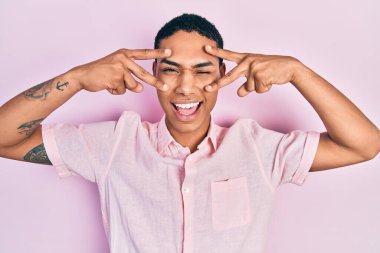 Genç Afrikalı Amerikalı adam zafer işareti yapıyor ve barış jesti kameraya seksi bir ifadeyle bakıyor, neşeli ve mutlu bir yüzle.. 