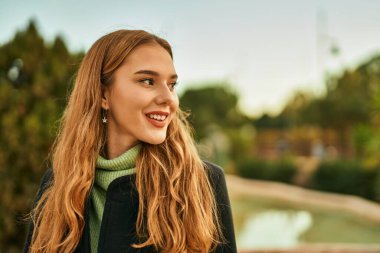 Genç sarışın kız gülümsüyor, mutlu bir şekilde şehirde duruyor..