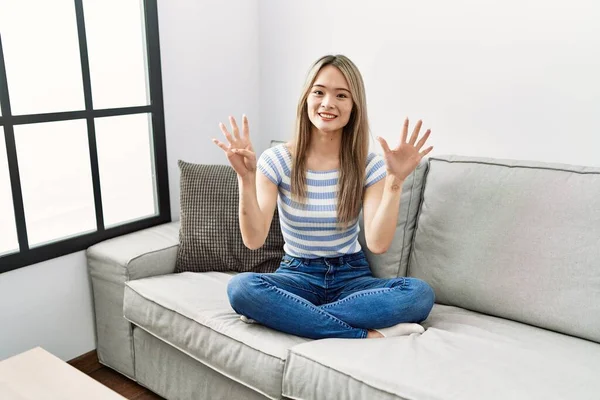 Asiática Jovem Mulher Sentada Sofá Casa Mostrando Apontando Para Cima — Fotografia de Stock