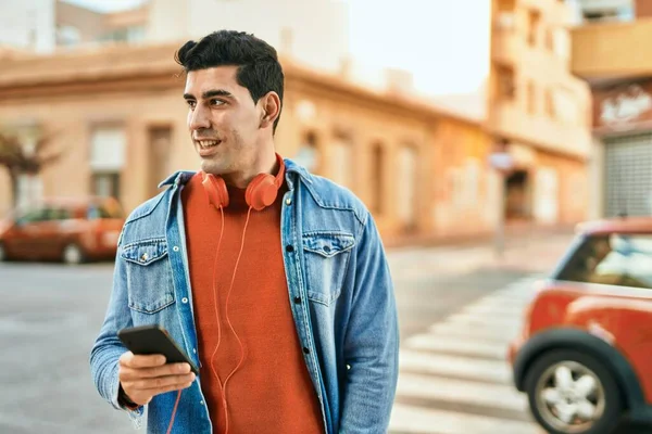 Young hispanic man smiling happy using smartphone and headphones at the city.