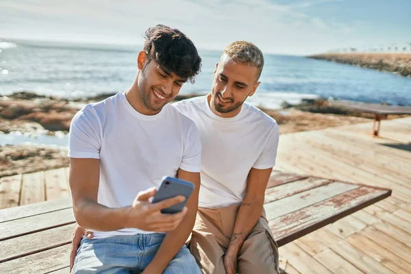 Νεαρό Γκέι Ζευγάρι Χαμογελά Χαρούμενος Χρησιμοποιώντας Smartphone Στην Παραλία Περιπάτους — Φωτογραφία Αρχείου