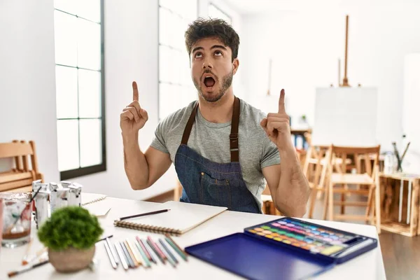 Jovem Hispânico Estúdio Arte Espantado Surpreso Olhando Para Cima Apontando — Fotografia de Stock