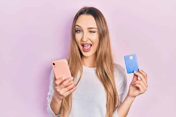 Młoda Blondynka Trzyma Smartfona Karty Kredytowej Mrugając Patrząc Aparat Seksownym — Zdjęcie stockowe