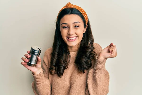 Young hispanic woman black pepper grinder screaming proud, celebrating victory and success very excited with raised arm