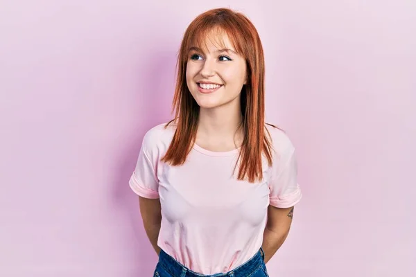 顔に笑みを浮かべて横に見てカジュアルなピンクのTシャツを着て赤毛の若い女性は 自然な表情 自信を持って — ストック写真