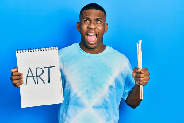 Joven Negro Sosteniendo Cuaderno Arte Pinceles Pintor Enojado Loco Gritando — Foto de Stock