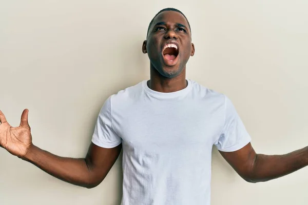 カジュアルな白いTシャツを着た若いアフリカ系アメリカ人の男性は 狂気と怒鳴り声を上げ 積極的な表現と腕を上げて叫びました フラストレーションコンセプト — ストック写真
