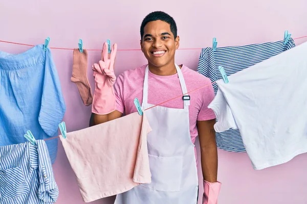 Jovem Homem Hispânico Bonito Vestindo Avental Mais Limpo Segurando Roupas — Fotografia de Stock