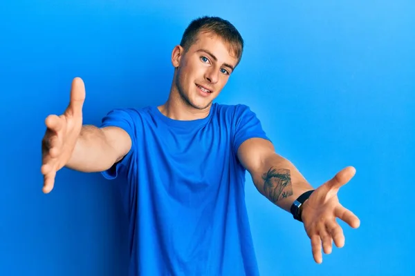 年轻的高加索男人穿着休闲的蓝色T恤 看着镜头 张开双臂拥抱 欢快的表达拥抱幸福 — 图库照片
