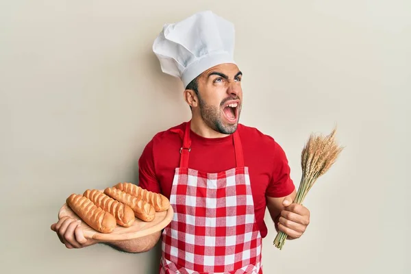 Mladý Hispánec Pekařské Uniformě Držící Domácí Chléb Pšenici Rozzlobený Šílený — Stock fotografie