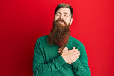 Uzun sakallı, sıradan kıyafetler giyen, göğsünde elleriyle gülümseyen, yüzünde minnet ifadesi olan kızıl saçlı bir adam. sağlık kavramı. 