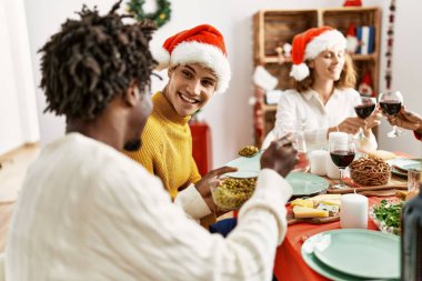 Bir grup genç, mutlu bir şekilde gülümseyerek evde Noel yemeği yiyor..