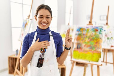 Sanat stüdyosundaki genç esmer kadın el pençe divan durup, sadakat yemini ederken gülümsüyor. 