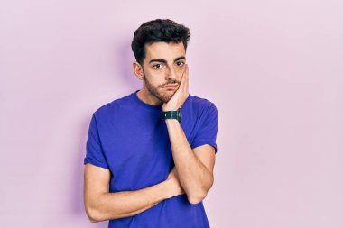 Günlük tişört giyen genç İspanyol adam kollarını kavuşturup depresyondan sıkılmış ve yorgun görünüyor.. 