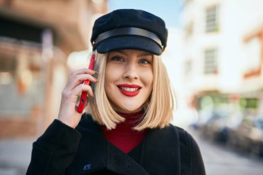 Genç sarışın kadın gülümsüyor. Şehirdeki akıllı telefondan konuşuyor..