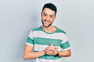 Latin asıllı genç adam ellerinin birleştiği günlük kıyafetler giyiyor ve gülümseyerek gevşemiş ve neşeli gülümsüyor. Başarı ve iyimserlik 
