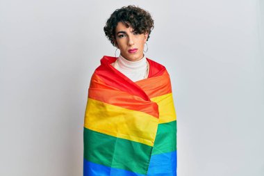 Gökkuşağı lgbtq bayrağına sarılı kadın makyajı yapan genç adam yüzünde ciddi bir ifadeyle rahatladı. Basit ve doğal bir şekilde kameraya bakıyorsun.. 