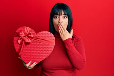 Genç İspanyol kadın sevgililer günü hediyesini tutarken ağzını eliyle kapatmış, şok olmuş ve hata yapmaktan korkan. şaşırmış ifade 