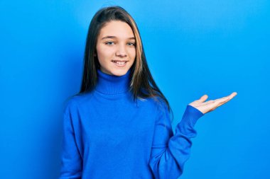 Balıkçı yaka kazak giyen genç esmer kız neşeli bir şekilde gülümsüyor ve avuç içi kameraya bakıyor.. 